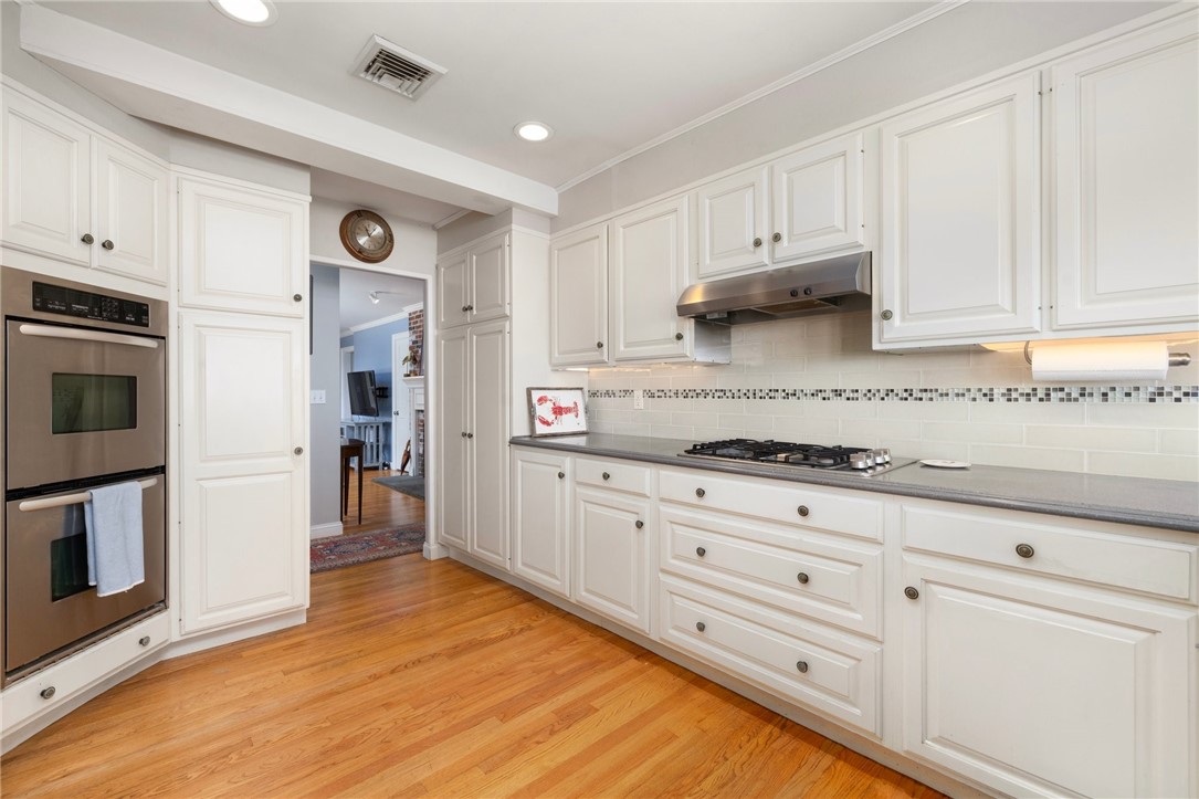 Kitchen with white cabinets, double wall ovens, a gas cooktop, and hardwood floors.