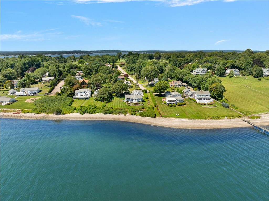 Aerial view of waterfront homes along a tree-lined shore, with lawns and a small dock.