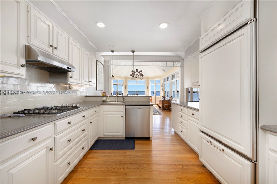 White kitchen with stainless appliances and hardwood floors, opening to a dining area with water views.