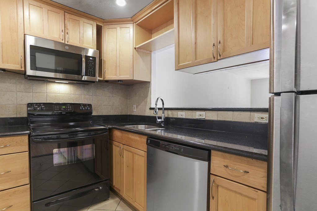 Kitchen with light wood cabinets, black countertops, and stainless-steel appliances.
