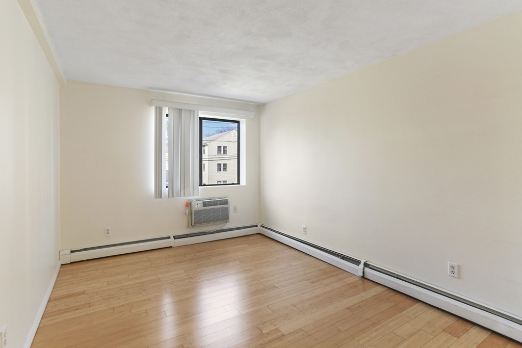 Empty room with light wood floors, baseboard heating, and a window air conditioner.