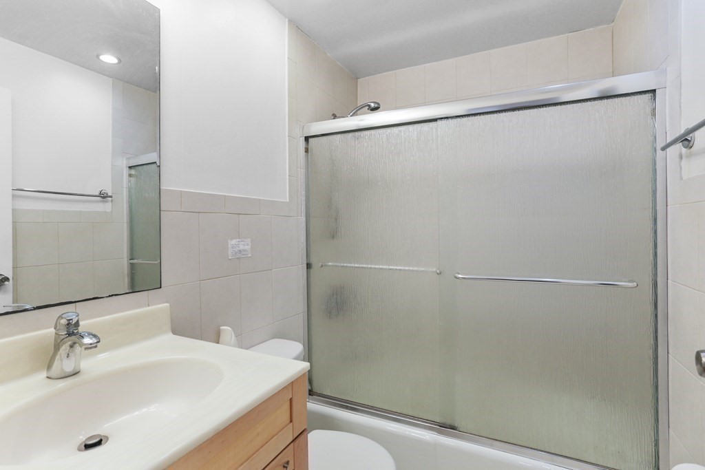 Bathroom with a wood vanity, large mirror, and frosted-glass tub and shower enclosure.