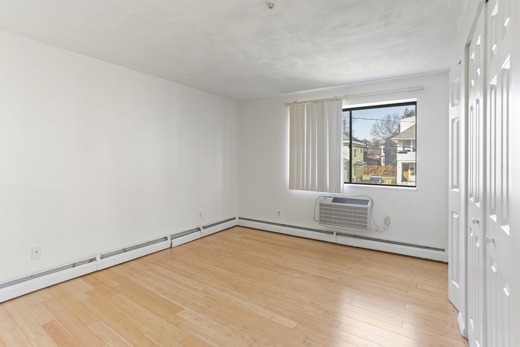 Empty room with light wood floors, closet doors, and a window air conditioner.