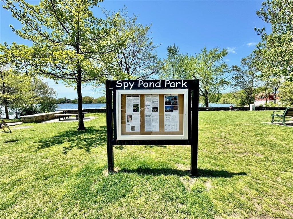 Spy Pond Park sign on a grassy lawn beside the pond.