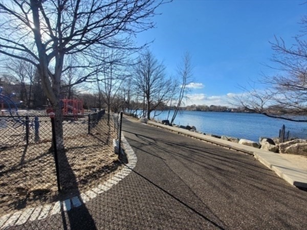 Pond-side path curving past shoreline rocks and leafless trees.