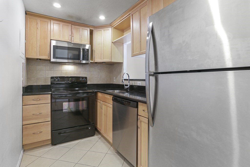 Compact kitchen with light wood cabinets, dark countertops, and stainless-steel appliances.