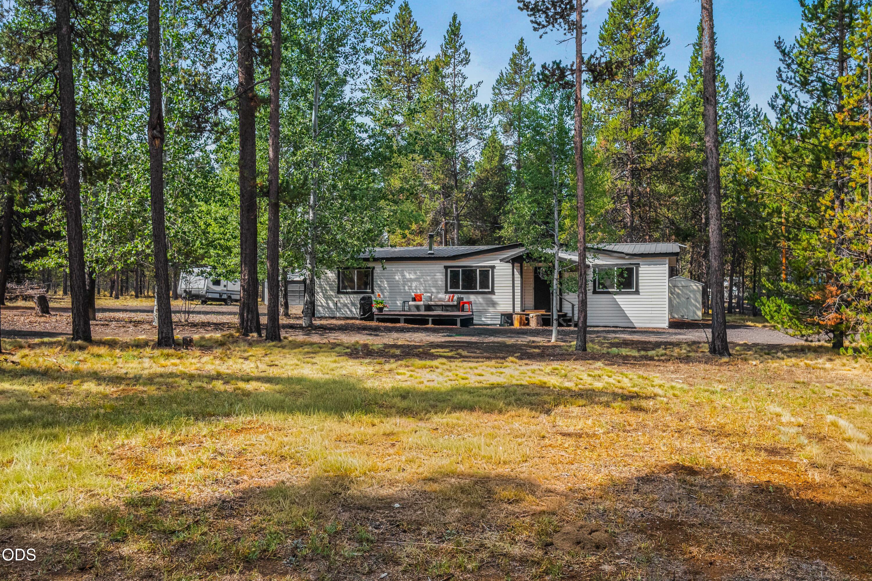 Single-story home with a small deck surrounded by tall pine trees.