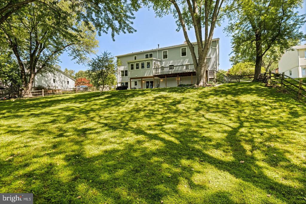 Rear of a two-story house above a broad, tree-shaded lawn, with a raised deck.