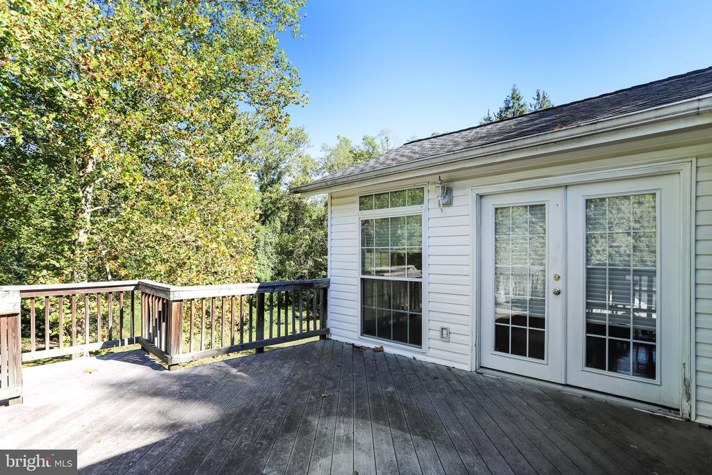 Rear deck with weathered wood flooring, railings, and glass doors overlooking mature trees.