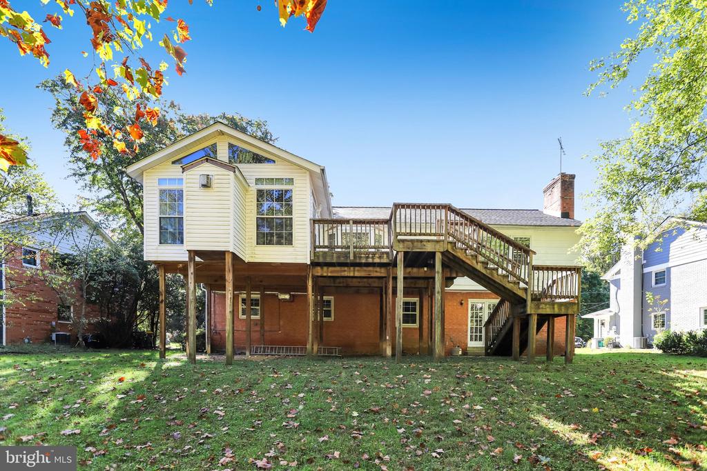 Rear of a two-story house with a raised wooden deck and long wooden staircase.