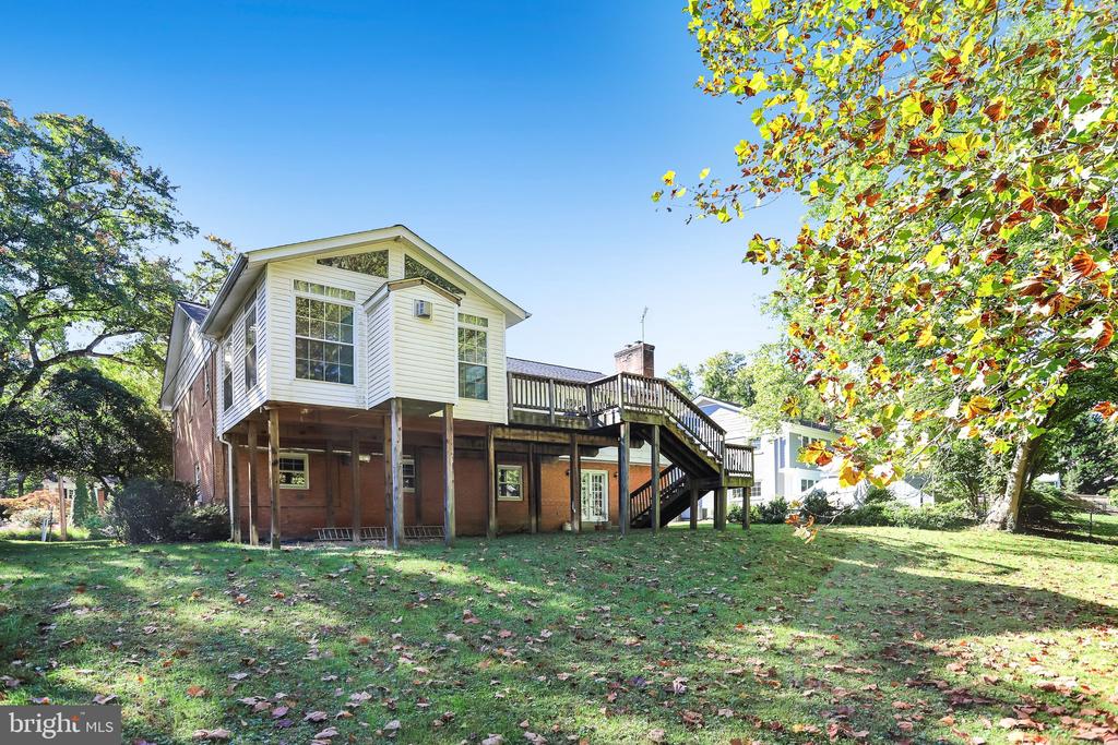 Rear of a two-story brick and white-sided home with a raised wooden deck and exterior stairs.