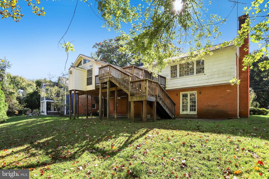 Rear of a two-story brick and yellow-sided house with an elevated wooden deck and leaf-strewn lawn.