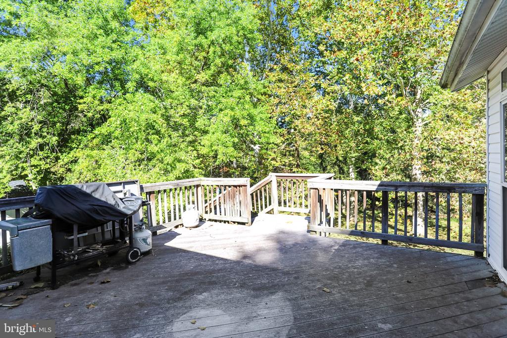 Wooden rear deck with railings and a covered grill, overlooking leafy trees.