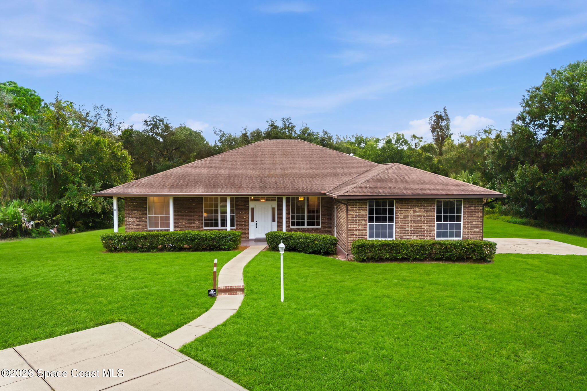 Single-story brick house with a hipped roof, curved front walkway, and expansive green lawn.