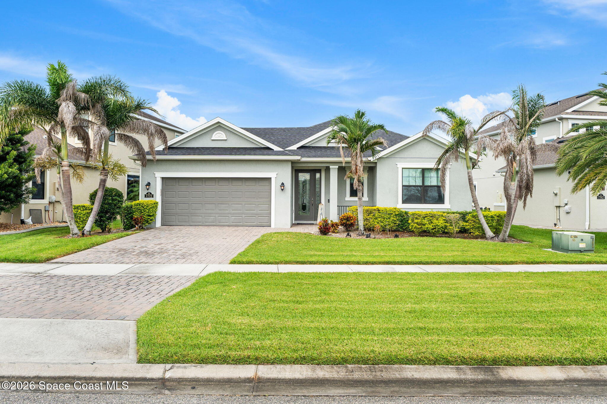 Single-story house with a two-car garage, palm trees, and a paved driveway.