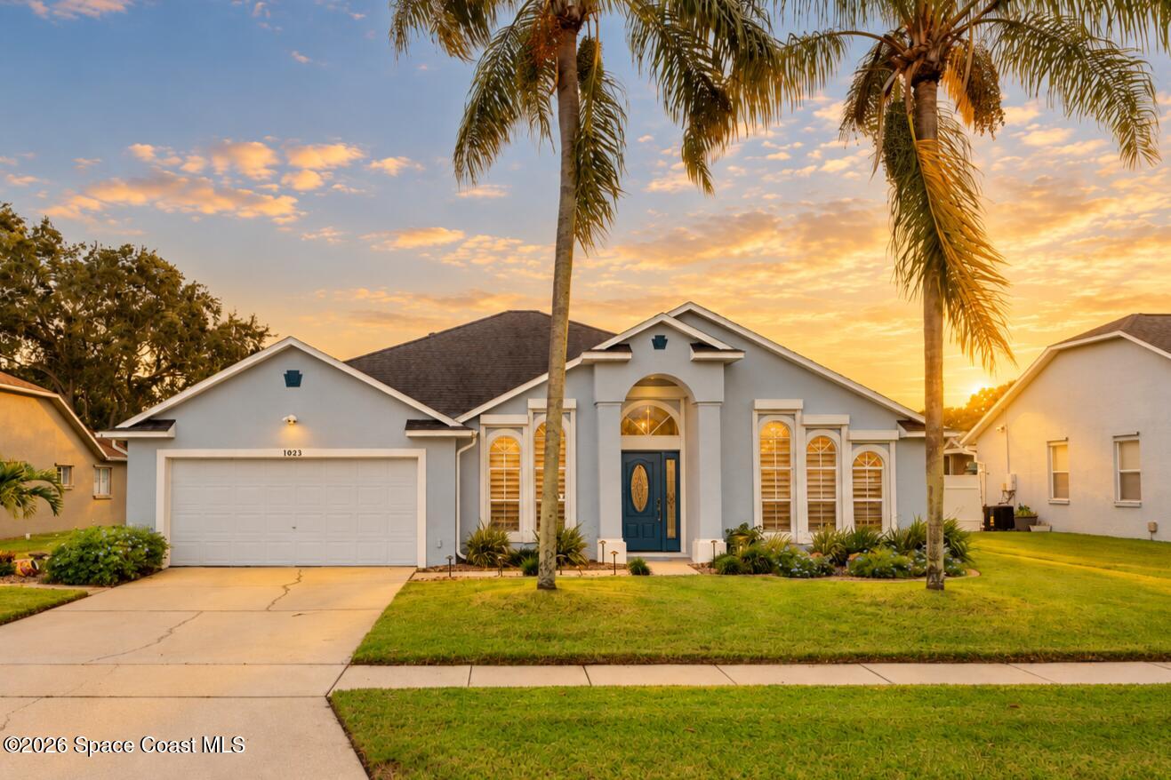 Single-story stucco home with a two-car garage, blue front door, and palm trees at sunset.