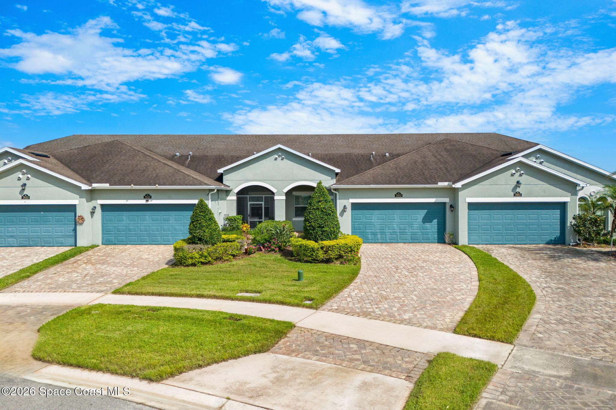 Attached homes with blue garage doors, brick-paver driveways, and landscaped front lawns.
