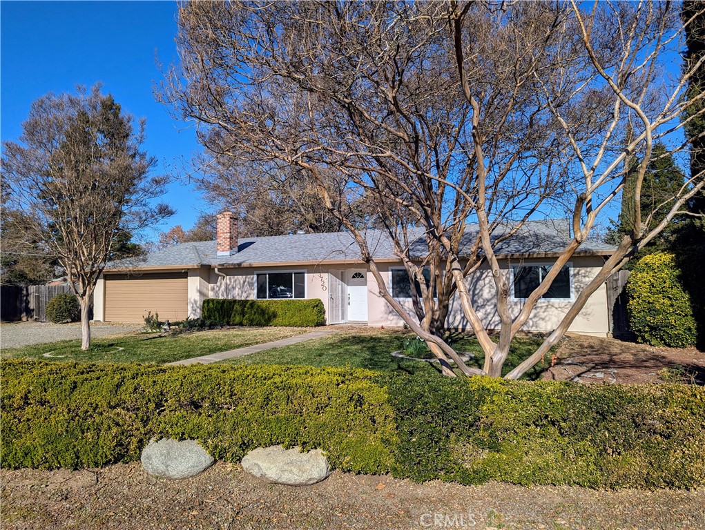 Single-story house with attached garage, brick chimney, and landscaped front yard beneath mature leafless trees.