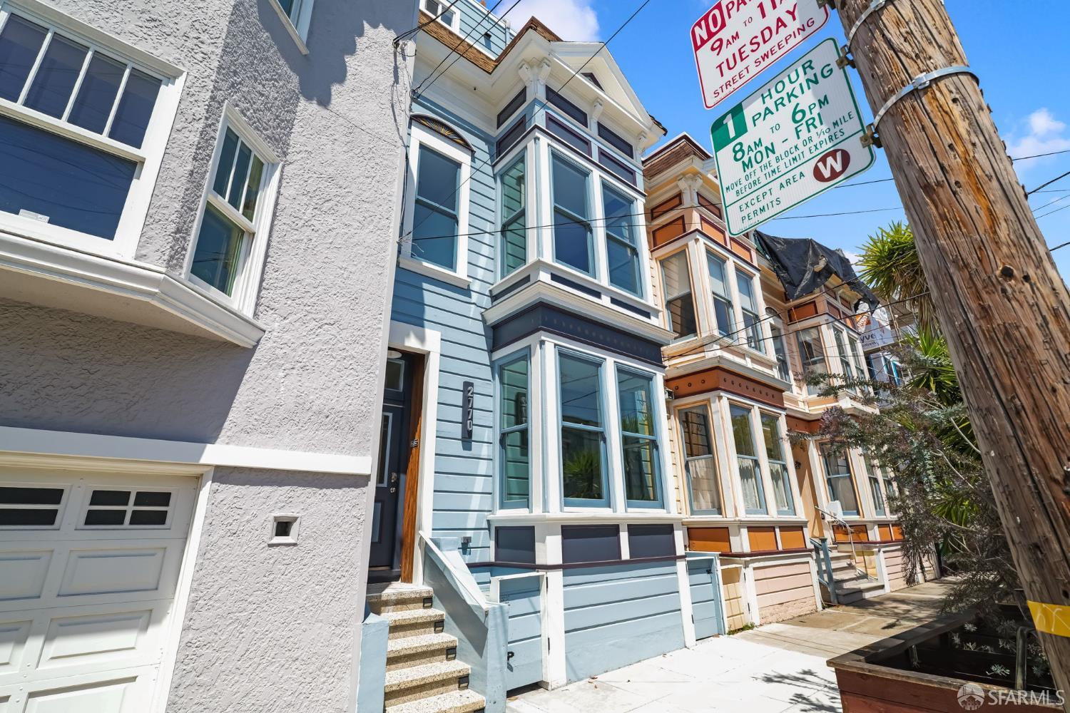 Blue multi-story townhouse with bay windows beside neighboring homes and street parking signs.