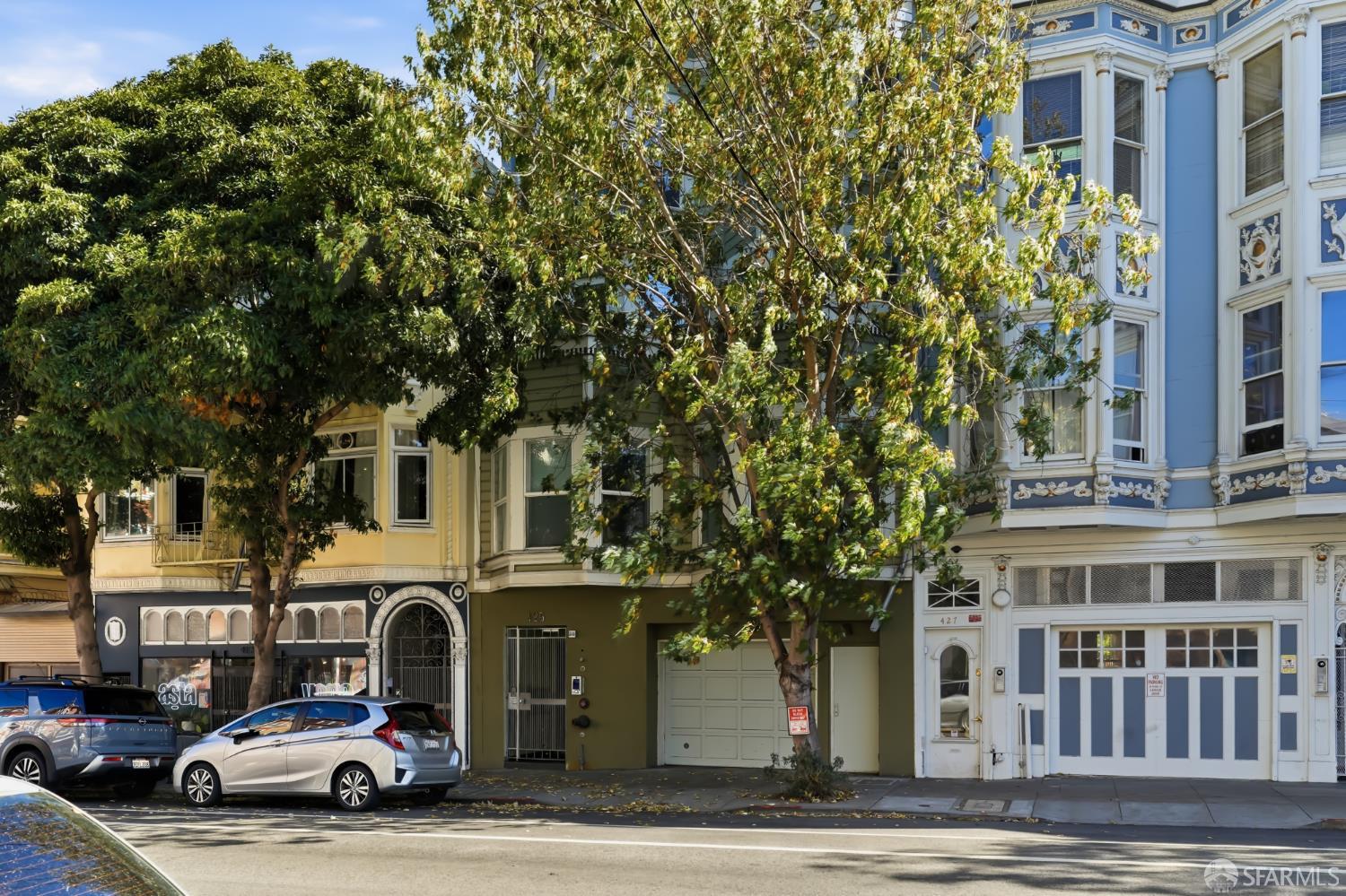 Green residential building at 425 beside an ornate blue Victorian, framed by leafy street trees.