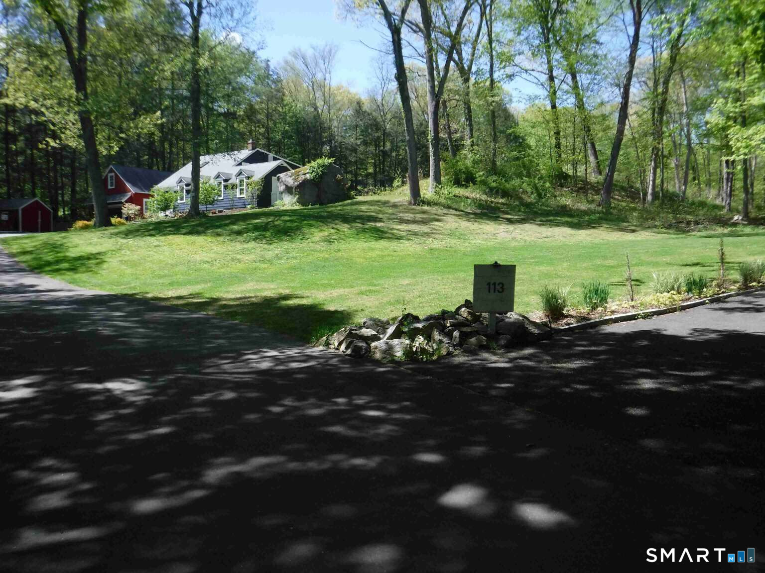 Gray-blue house among mature trees, with a broad lawn and roadside sign marked 113.