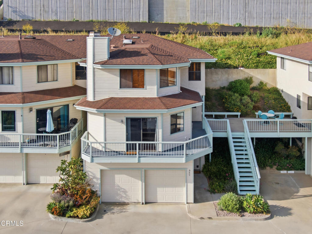 Two-story home with wraparound balconies, twin garage doors, and a raised patio with outdoor dining.