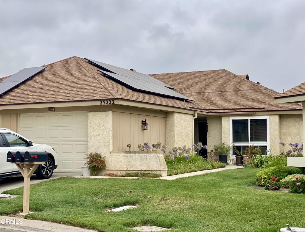 Single-story tan home with rooftop solar panels, an attached garage, and a green front lawn.