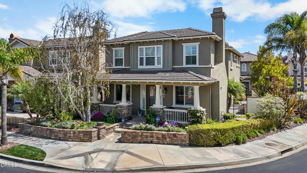 Two-story gray home with a covered porch, flowering garden, and stone planters.