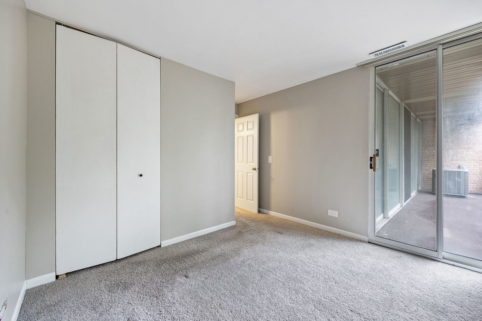 Empty carpeted bedroom with a wall closet and sliding glass doors to a covered balcony.