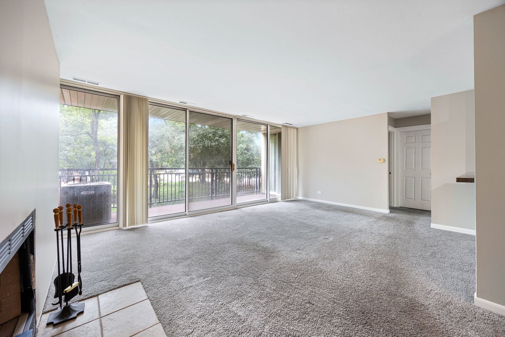 Vacant living room with sliding glass doors to a balcony and leafy views.