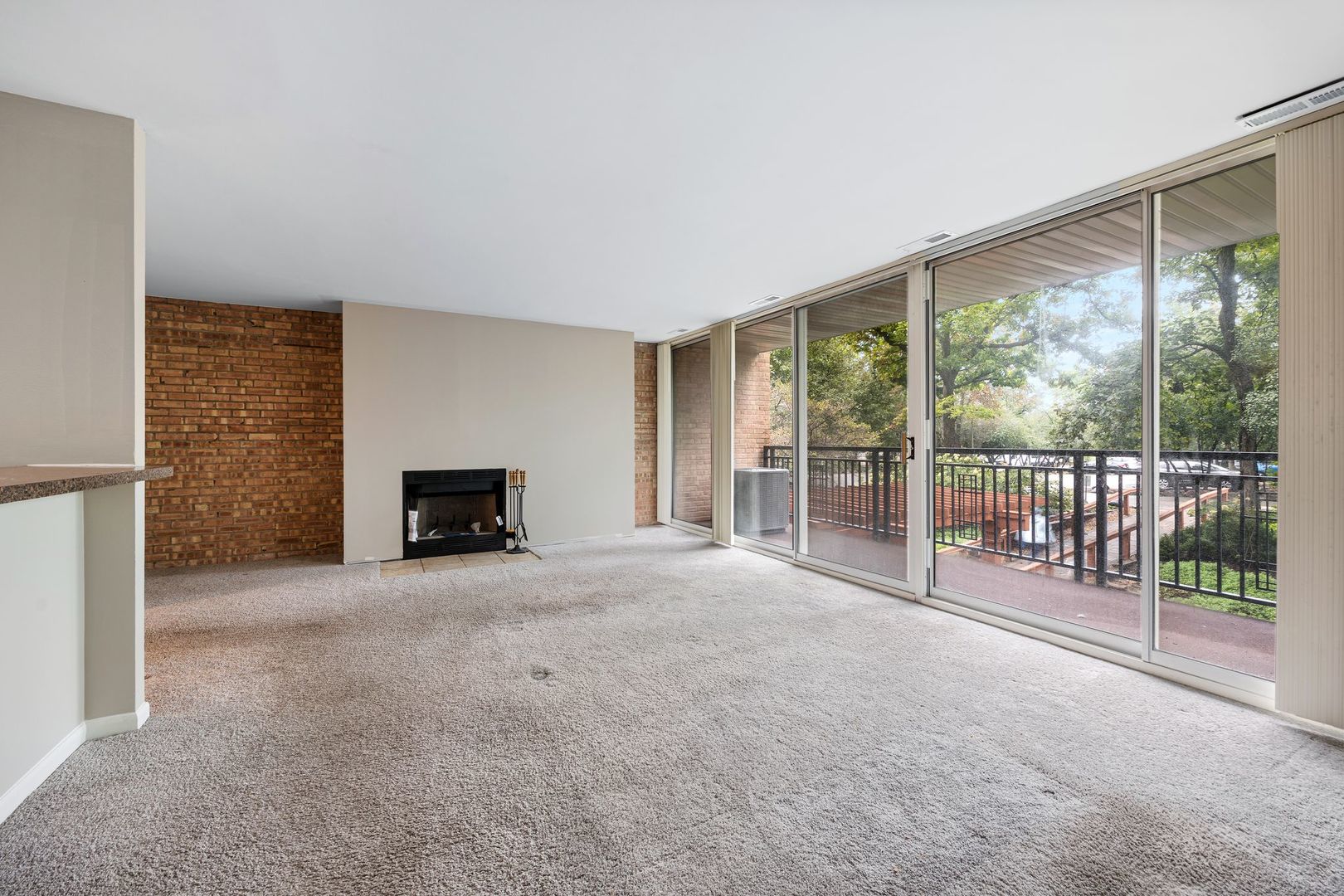 Empty living room with a brick fireplace and floor-to-ceiling glass doors opening onto a balcony.