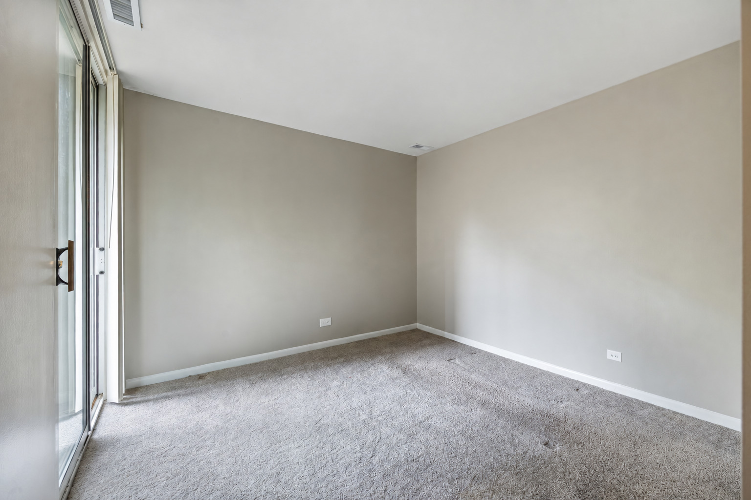Empty carpeted room with beige walls and a sliding glass door.