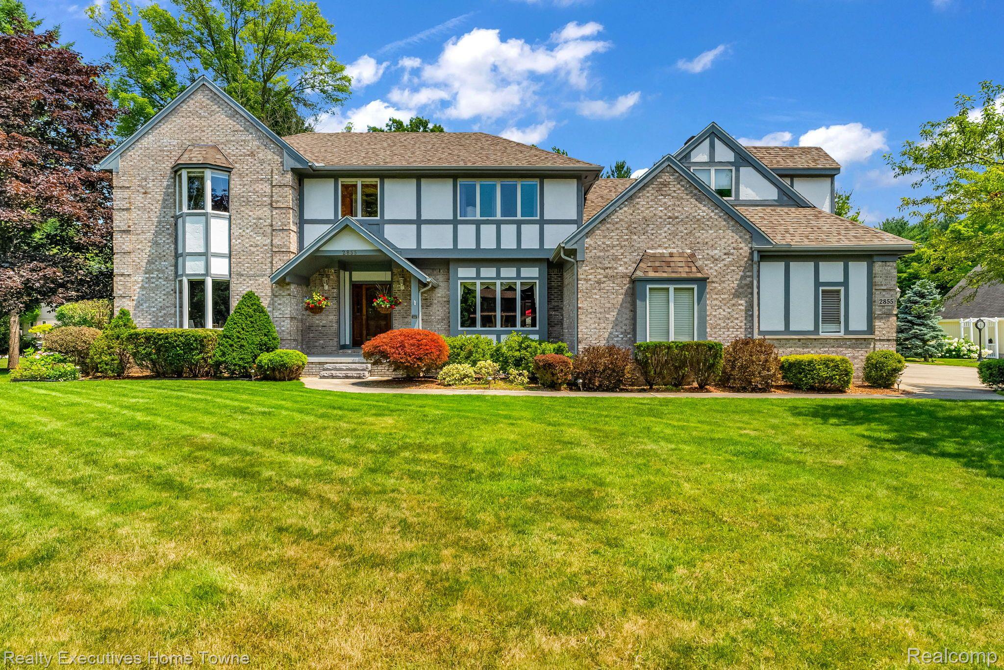Two-story brick-and-timber house with a broad lawn and landscaped shrubs.