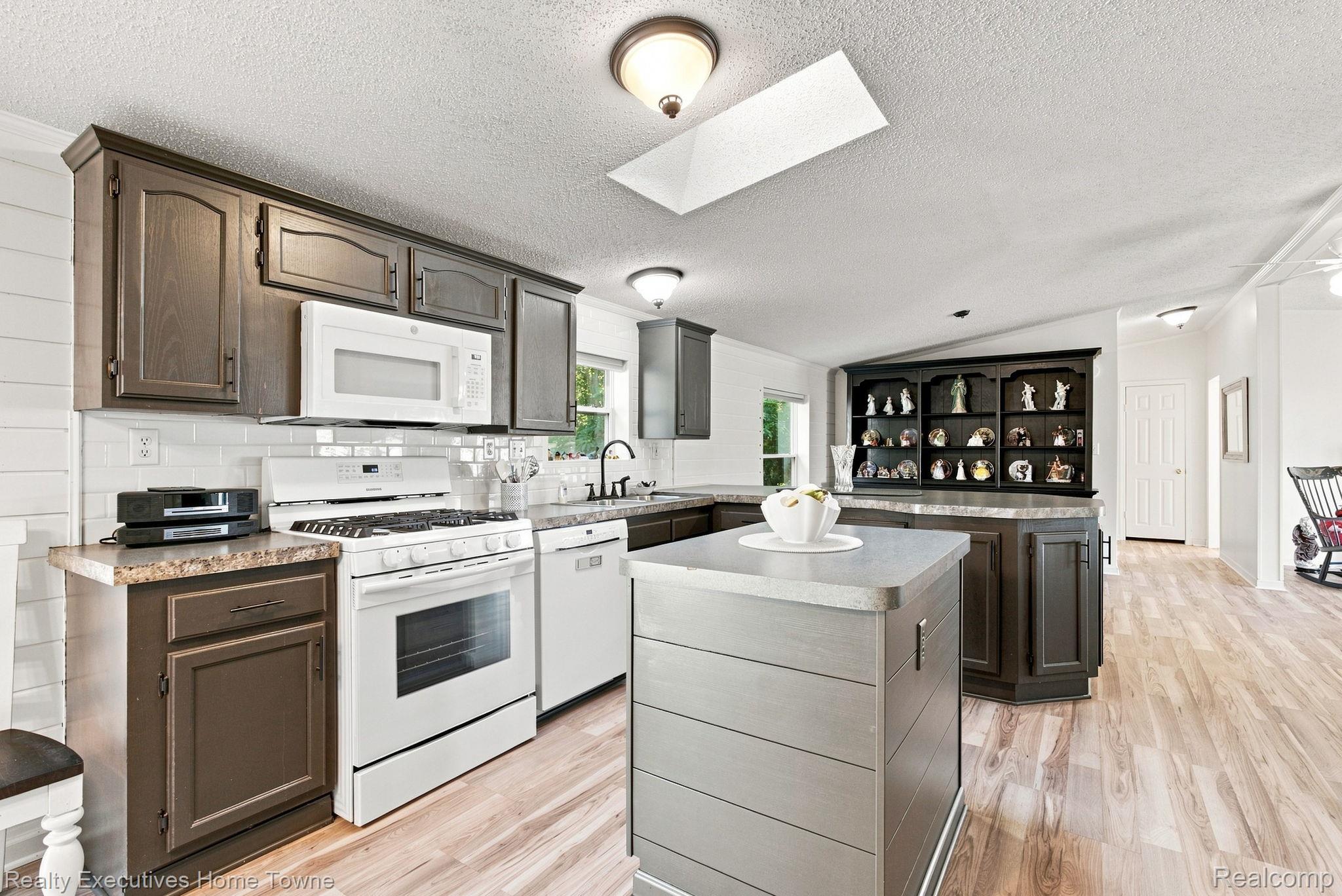 Kitchen with dark cabinets, white appliances, a central island, and a cabinet displaying figurines.