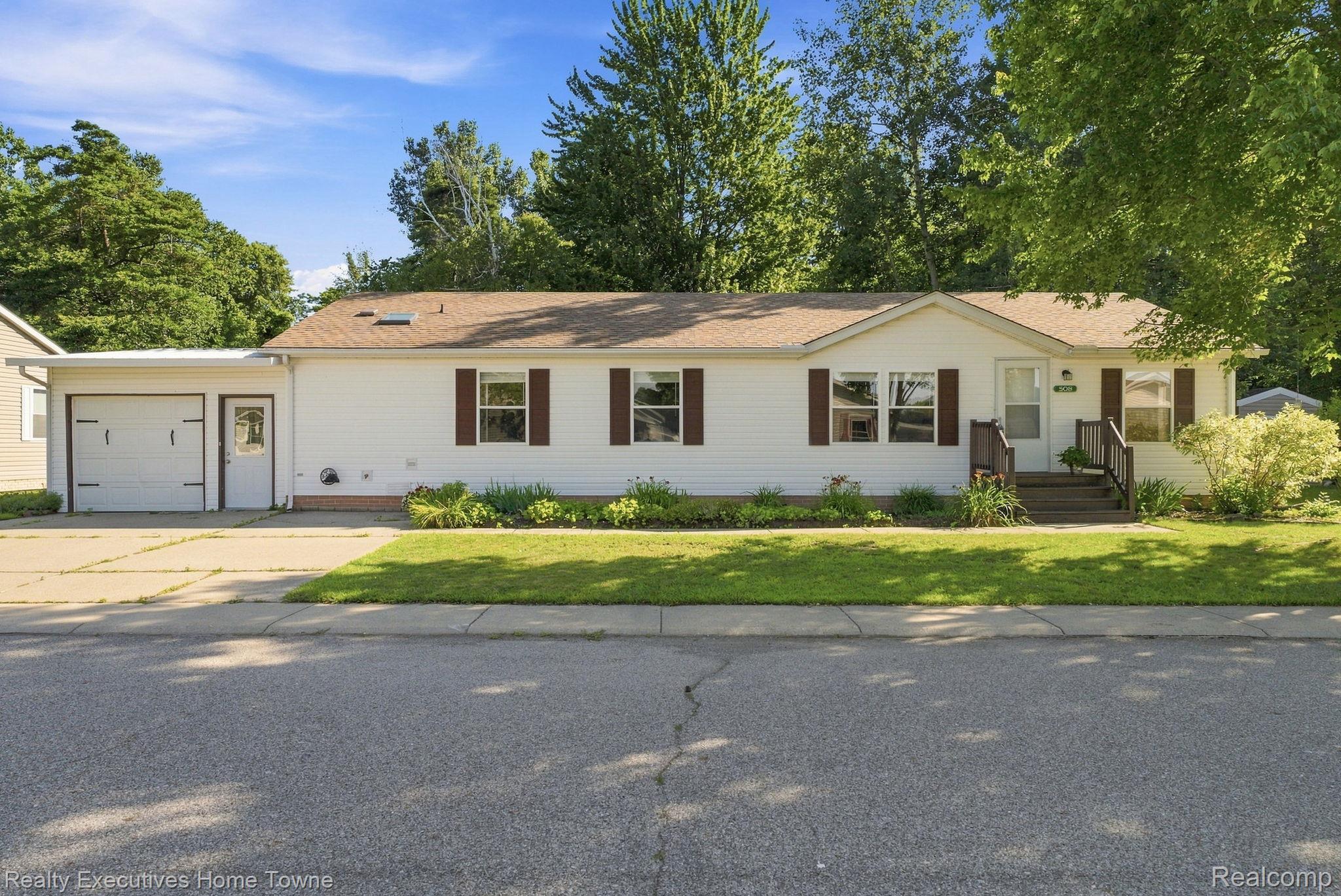 Single-story white house with an attached garage, brown shutters, and a tree-shaded front lawn.