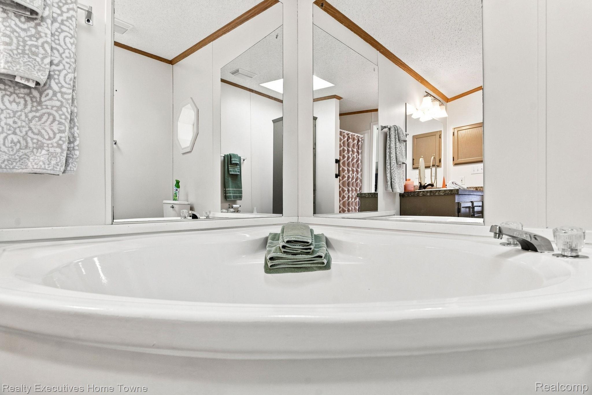 Bathroom vanity with a large oval sink, folded green towels, and mirrored walls.
