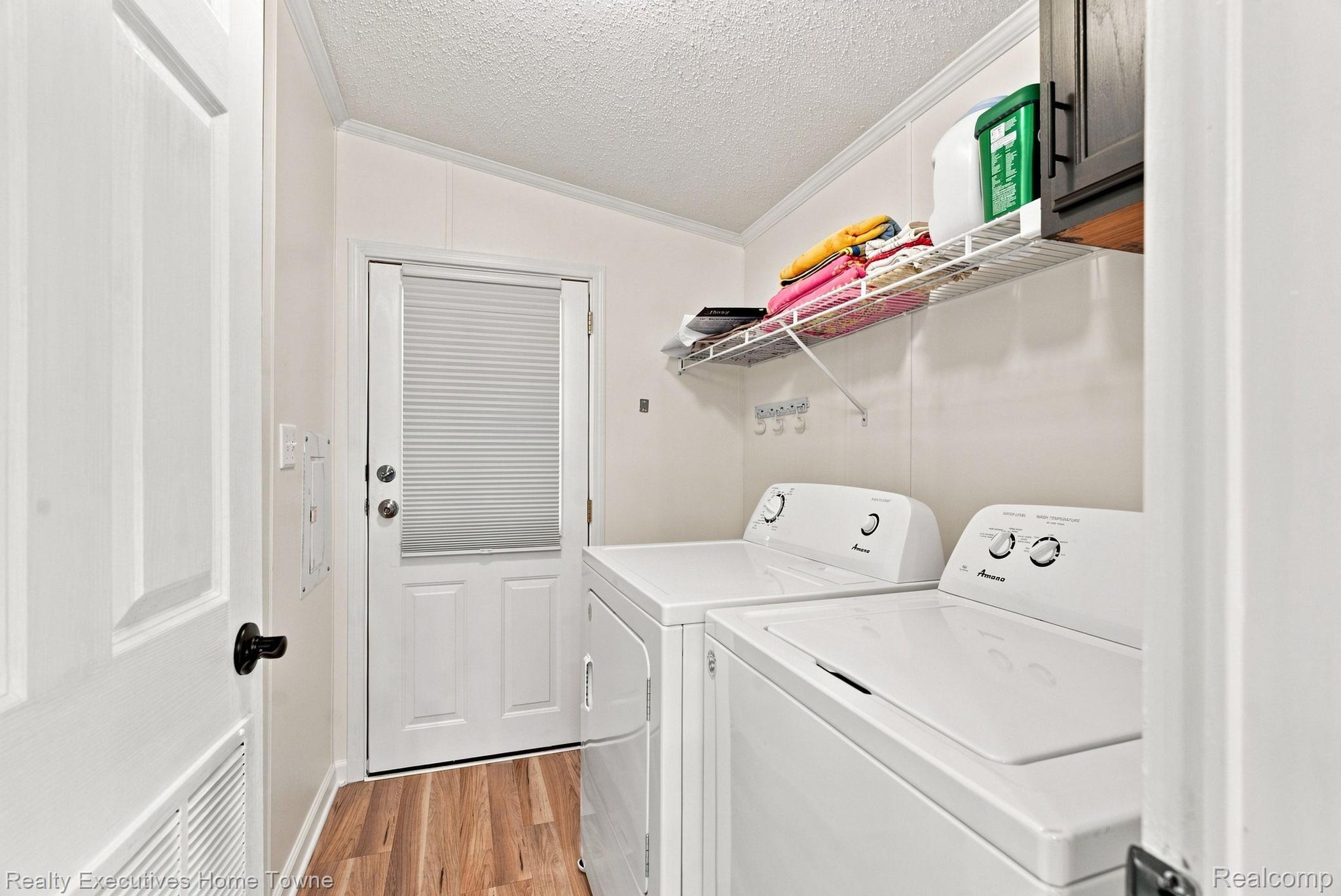Laundry room with a washer and dryer, wire shelving, folded towels, and wood-look flooring.