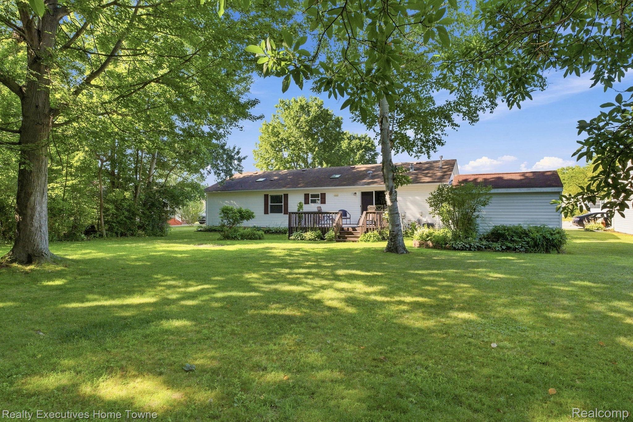 Rear of a white single-story home with a wooden deck, attached garage, and expansive shaded lawn.