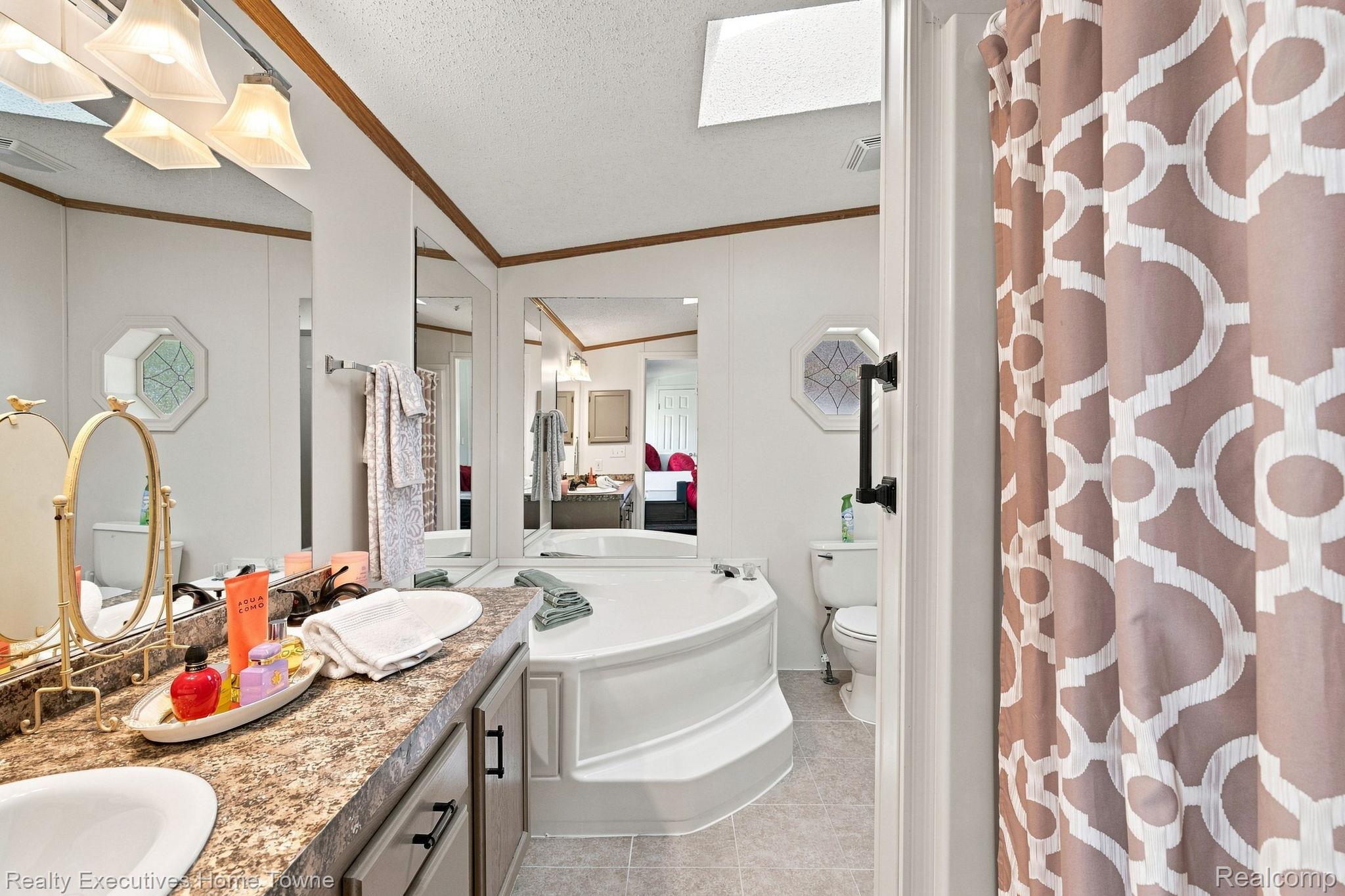 Bathroom with a corner soaking tub, granite double vanity, and patterned shower curtain.