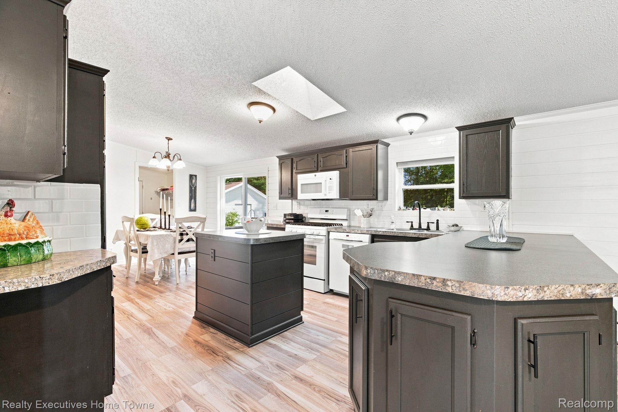 Kitchen with dark cabinetry, two large islands, white appliances, and an adjoining dining area.