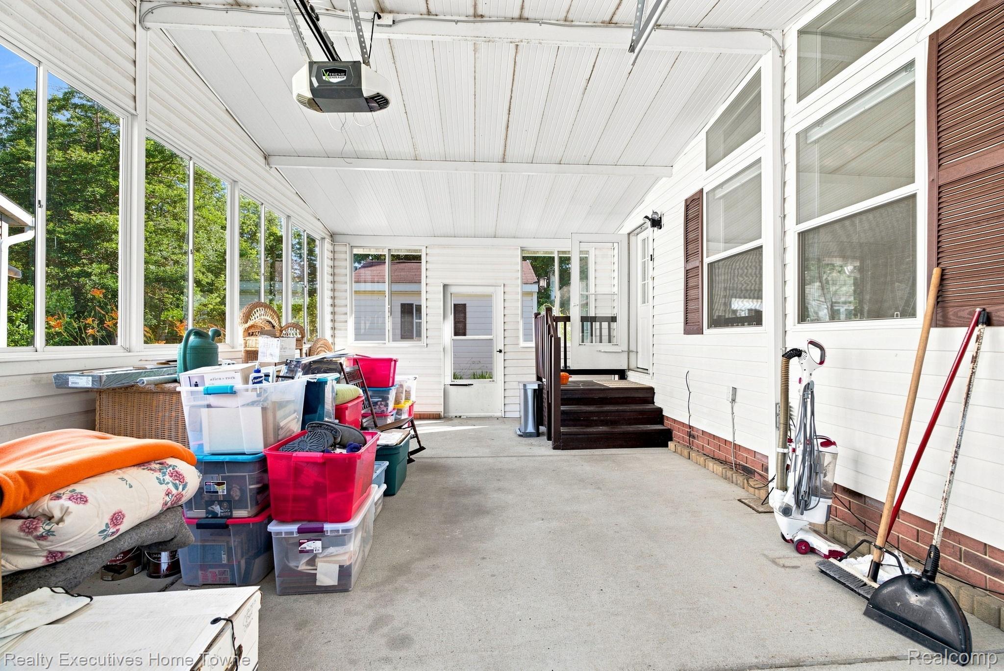 Enclosed porch with large windows, a concrete floor, and household storage bins along one side.