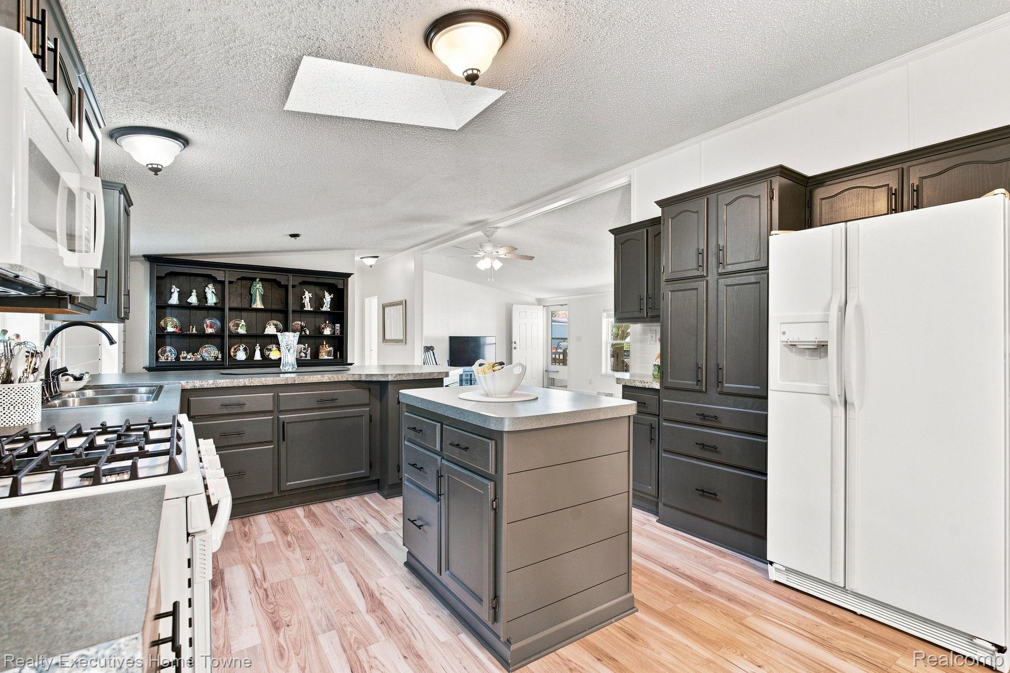 Kitchen with dark cabinetry, a large island, white appliances, and a built-in display shelf.