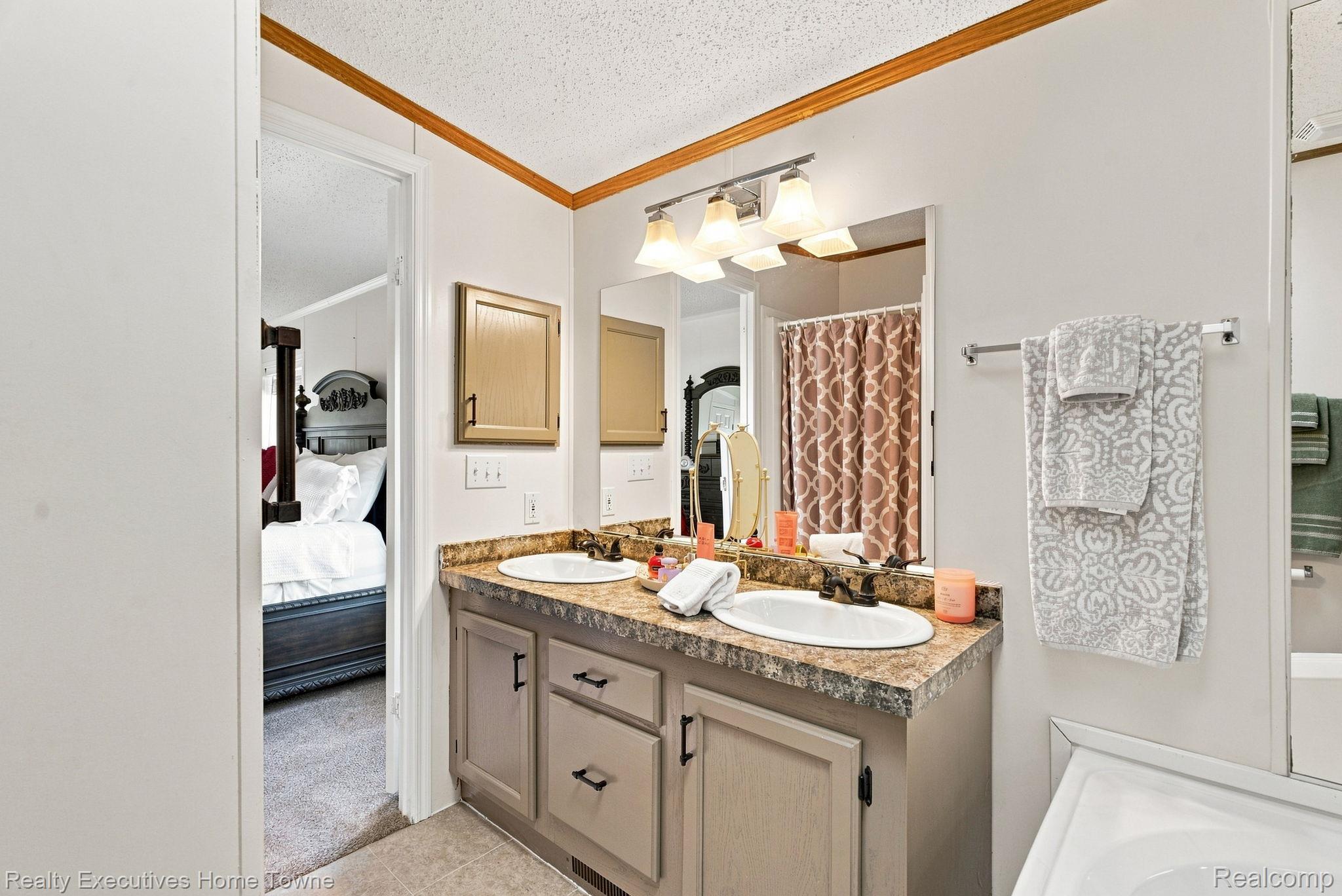 Bathroom with a double-sink vanity and stone countertop, with a bedroom visible through the open doorway.