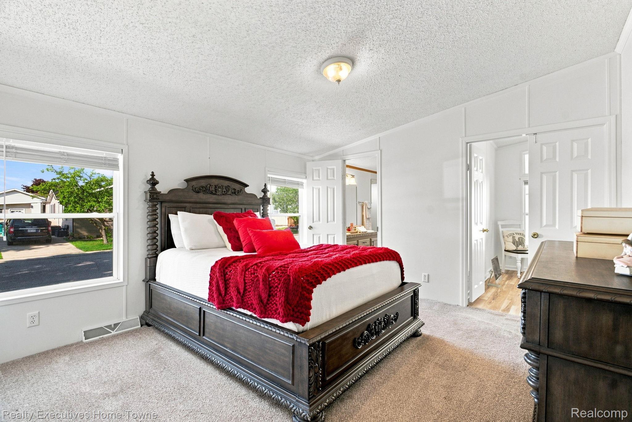 Bedroom with an ornate dark wood bed dressed in white bedding and vivid red accents.