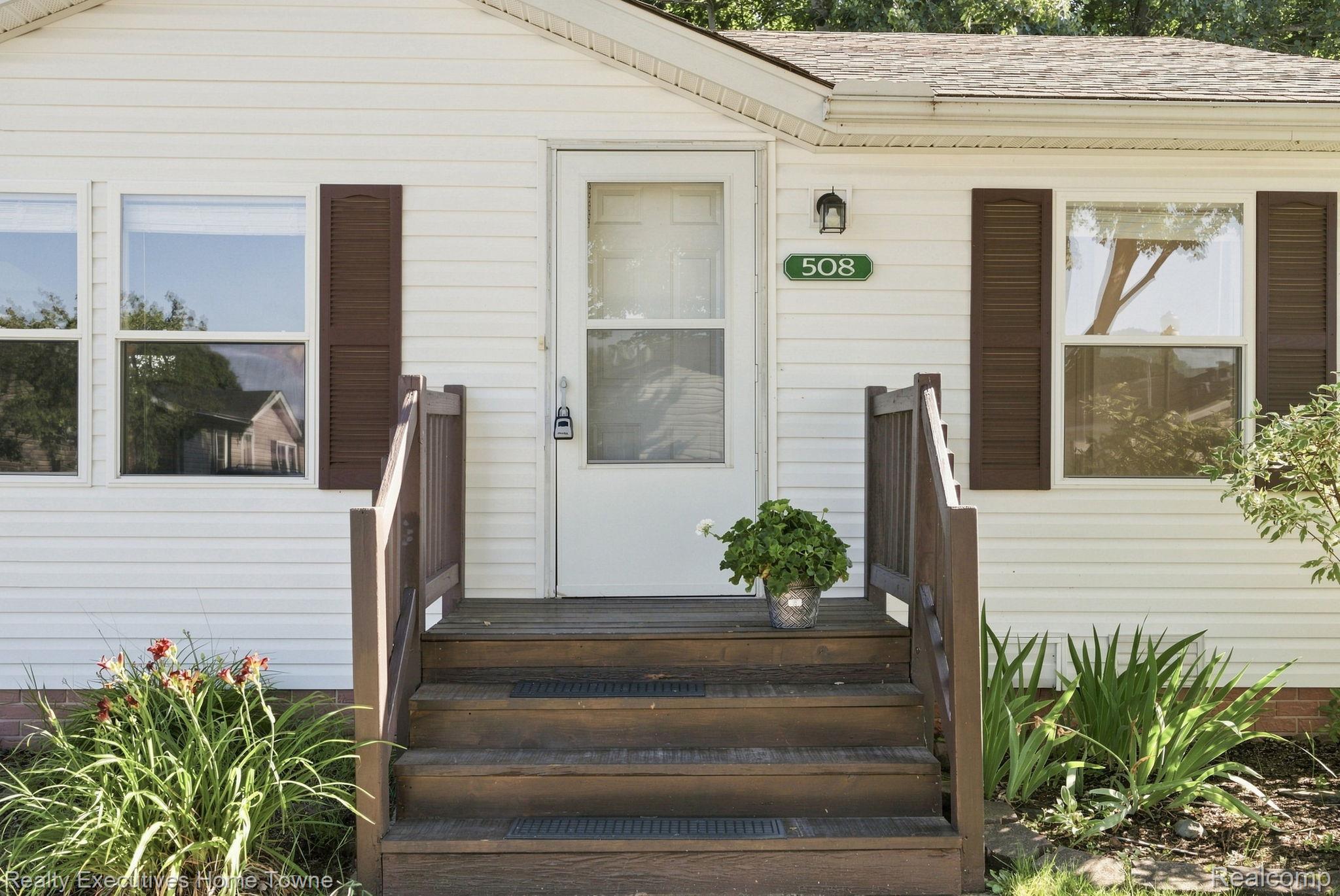 House entrance with a green 508 address plaque, dark wooden steps, and a potted plant.