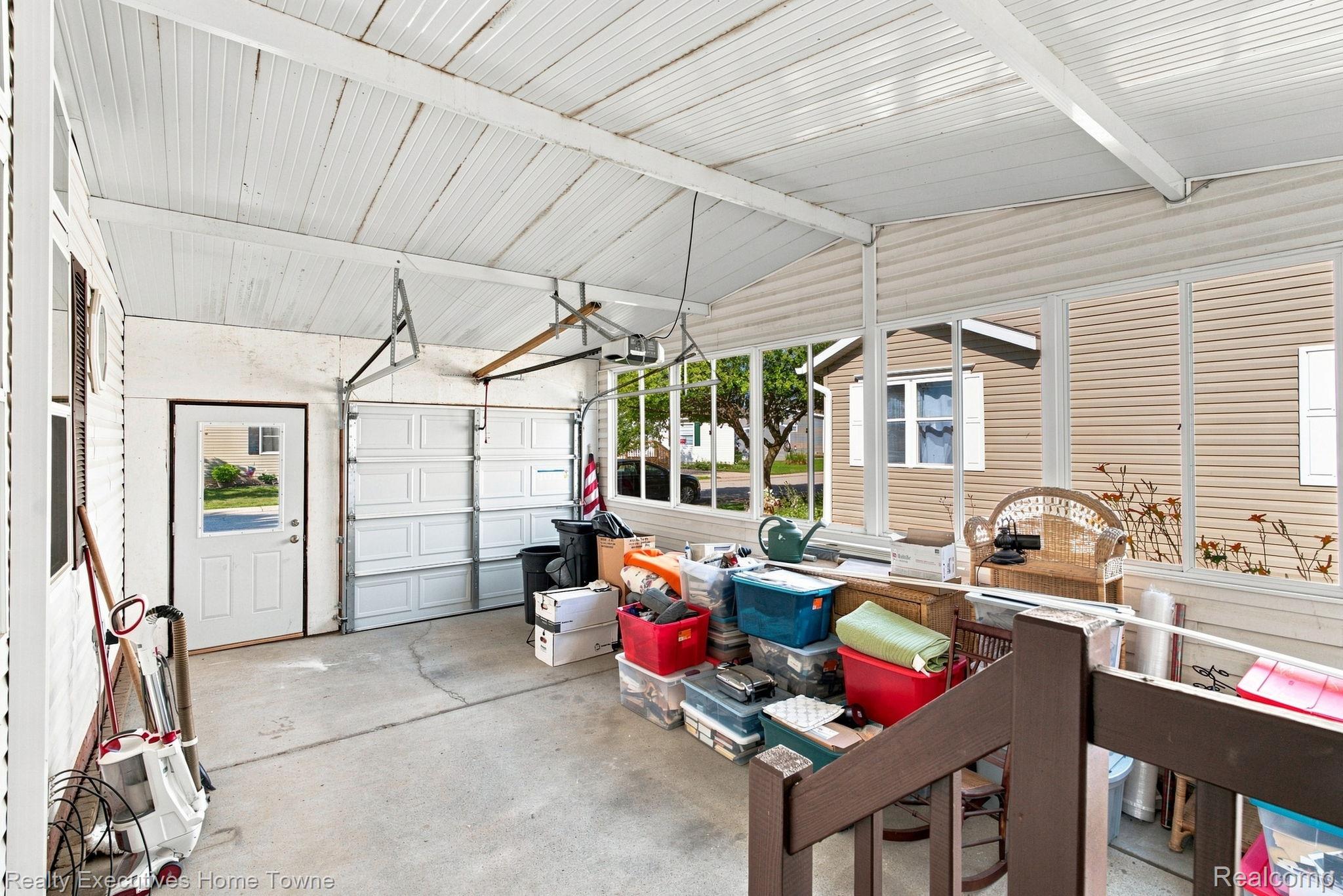 Enclosed garage with a concrete floor, overhead garage door, large windows, and stored bins and furniture.