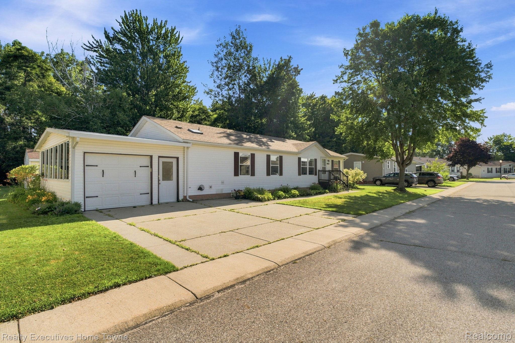 White single-story home with an attached garage and glass-enclosed sunroom beside a tree-lined street.