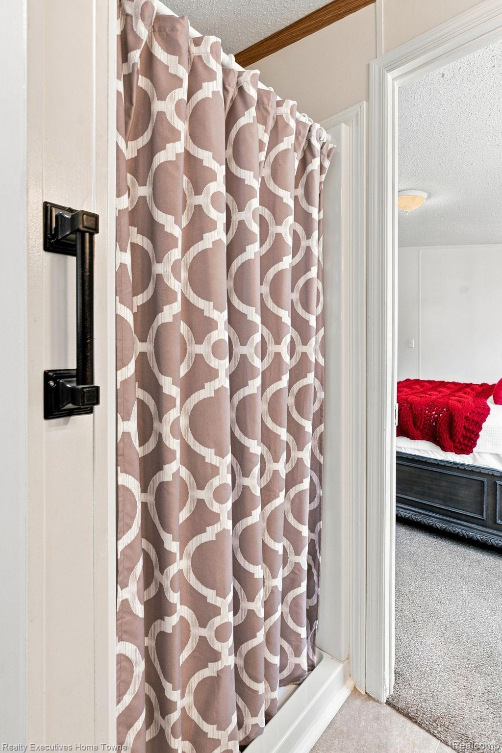 Bathroom shower with a geometric mauve curtain, opening onto a bedroom with red bedding.