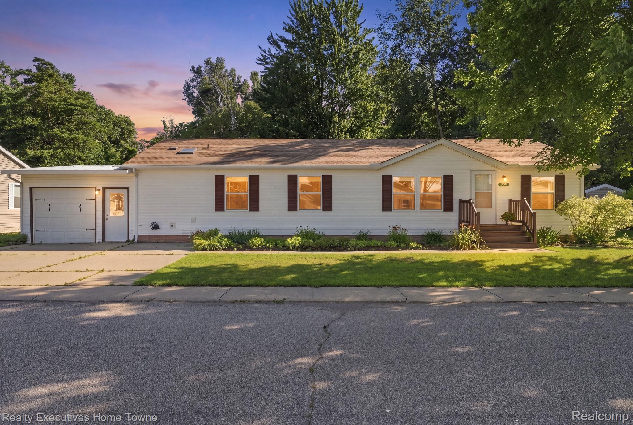 Single-story home with attached garage, landscaped front garden, and warm evening light in its windows.