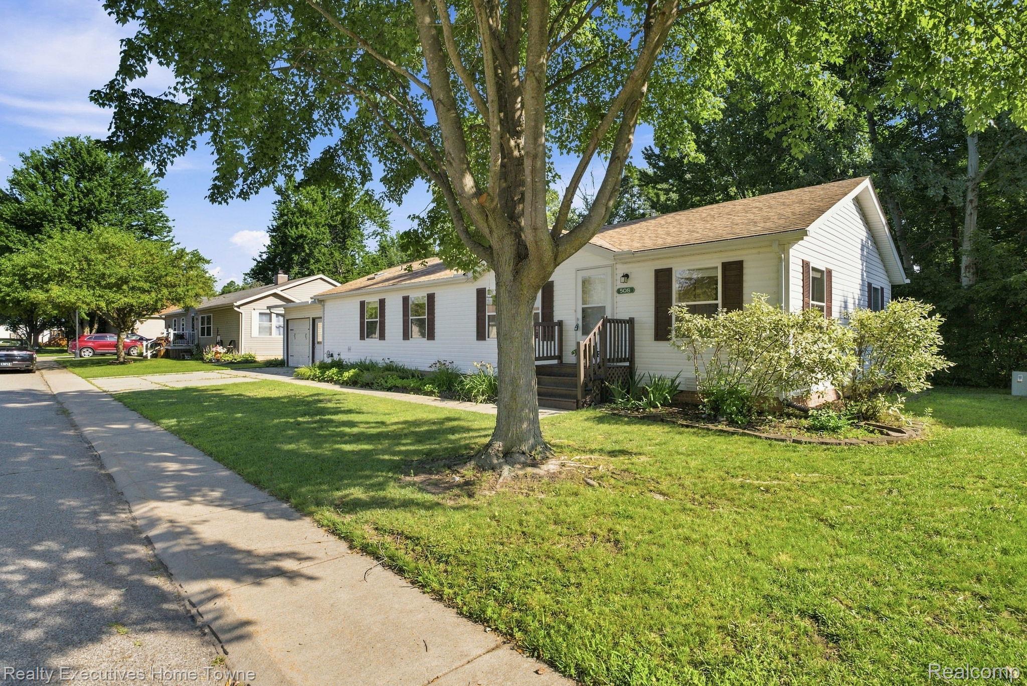 White single-story home with dark shutters and a front porch, shaded by a large mature tree.